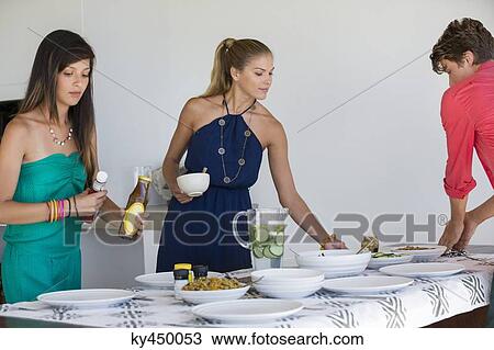 Friends arranging plates on a dining table View Large Photo Image Stock Image - Friends arranging plates on a dining table. Fotosearch