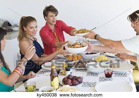 Friends passing food bowls at dining table View Large Photo Image Stock Photo - Friends passing food bowls at dining table. Fotosearch