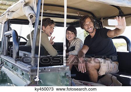 Stock Image - Friends taking picture of themselves with a mobile phone in a SUV. Fotosearch