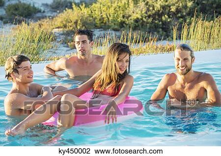 Stock Image - Group of friends enjoying in a swimming pool on the beach. Fotosearch