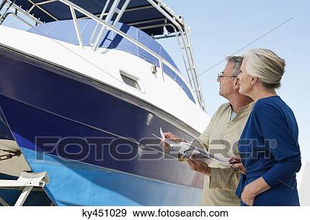 Couple standing near a yacht with a brochure View Large Photo Image Stock Photo - Couple standing near a yacht with a brochure. Fotosearch