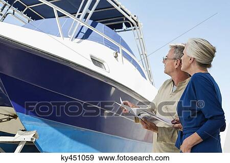 Couple standing near a yacht with a brochure View Large Photo Image Stock Photo - Couple standing near a yacht with a brochure. Fotosearch