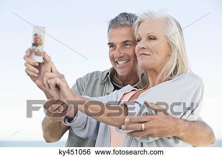 Couple taking a picture of themselves with a cell phone on the beach View Large Photo Image Stock Photograph - Couple taking a picture of themselves with a cell phone on the beach. Fotosearch
