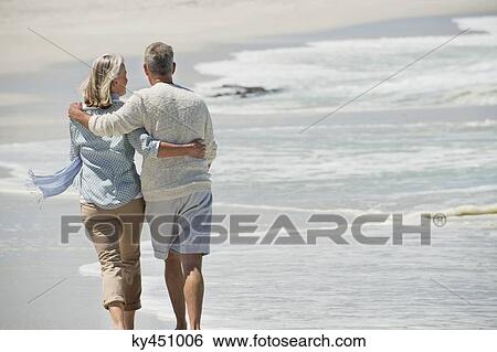 Rear view of a couple walking on the beach View Large Photo Image Stock Photograph - Rear view of a couple walking on the beach. Fotosearch