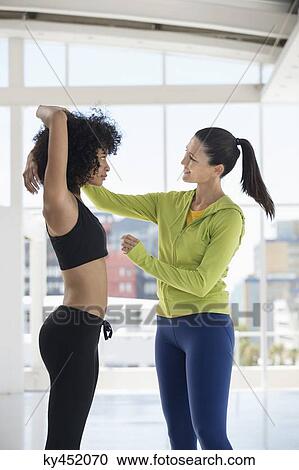 Female instructor assisting a woman in a gym View Large Photo Image Stock Image - Female instructor assisting a woman in a gym. Fotosearch