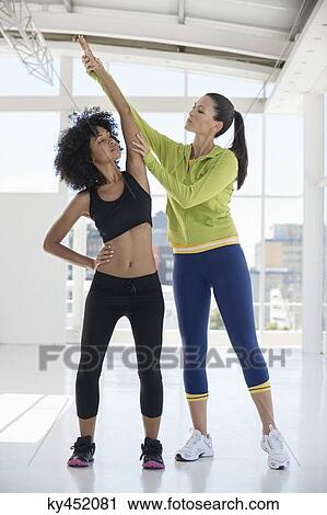 Female instructor assisting a woman in a gym View Large Photo Image Stock Image - Female instructor assisting a woman in a gym. Fotosearch