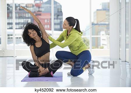 Stock Image - Female instructor assisting a woman in a gym. Fotosearch