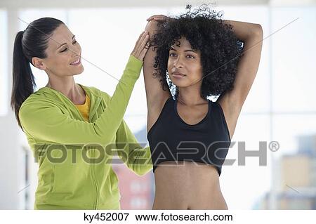 Stock Photo - Female instructor assisting a woman in a gym. Fotosearch