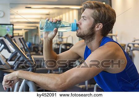 Man drinking water from a bottle at a gym View Large Photo Image Stock Image - Man drinking water from a bottle at a gym. Fotosearch