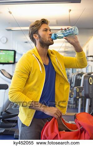 Man drinking water from a bottle in a gym View Large Photo Image Stock Photography - Man drinking water from a bottle in a gym. Fotosearch