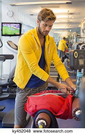 Stock Photo - Man packing his bag in a gym after workout. Fotosearch