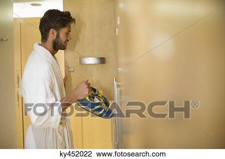 Stock Image - Man putting his shoes in a locker room at spa. Fotosearch