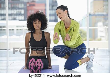 Stock Image - Woman practicing yoga with the help of an instructor. Fotosearch