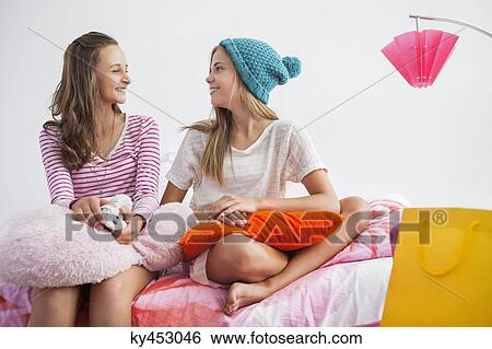 Stock Photograph - Girls sitting on the bed and talking to each other at a slumber party. Fotosearch