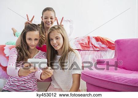 Three girls taking a picture of themselves with a mobile phone at a slumber party View Large Photo Image Stock Image - Three girls taking a picture of themselves with a mobile phone at a slumber party. Fotosearch