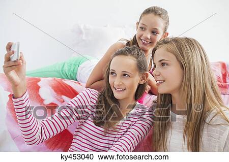 Stock Image - Three girls taking a picture of themselves with a mobile phone at a slumber party. Fotosearch