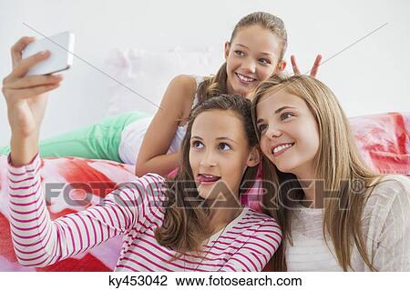 Stock Image - Three girls taking a picture of themselves with a mobile phone at a slumber party. Fotosearch