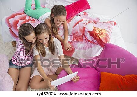 Three girls using a digital tablet at a slumber party View Large Photo Image Picture - Three girls using a digital tablet at a slumber party. Fotosearch