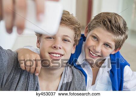Stock Photo - Two teenage boys taking a picture of themselves with a mobile phone. Fotosearch