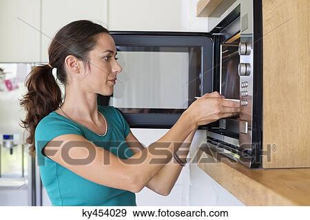 Stock Photo - Woman putting food into an oven. Fotosearch