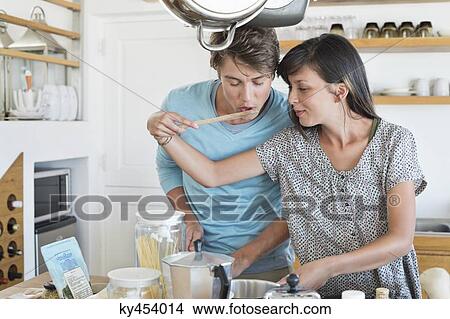 Woman tasting food to her husband in the kitchen View Large Photo Image Picture - Woman tasting food to her husband in the kitchen. Fotosearch