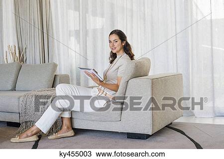 Beautiful woman using a digital tablet and smiling on a couch View Large Photo Image Stock Image - Beautiful woman using a digital tablet and smiling on a couch. Fotosearch