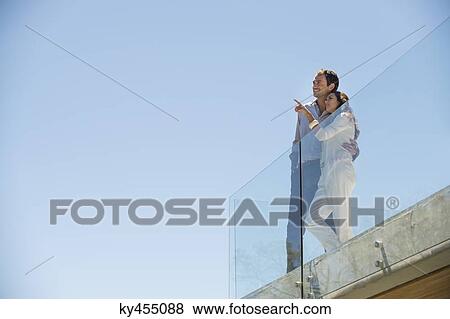 Couple standing together on a terrace and pointing away View Large Photo Image Stock Photo - Couple standing together on a terrace and pointing away. Fotosearch