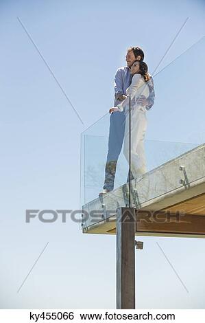 Couple standing together on a terrace and smiling View Large Photo Image Stock Photograph - Couple standing together on a terrace and smiling. Fotosearch