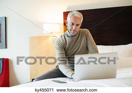 Man using a laptop in a hotel room View Large Photo Image Stock Image - Man using a laptop in a hotel room. Fotosearch