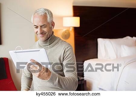Man watching a movie on digital tablet in a hotel room View Large Photo Image Stock Photograph - Man watching a movie on digital tablet in a hotel room. Fotosearch
