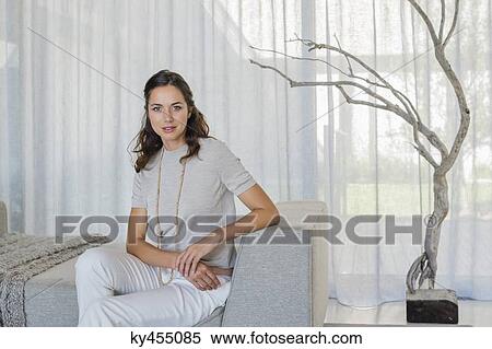 Portrait of a beautiful woman sitting on a couch View Large Photo Image Stock Photography - Portrait of a beautiful woman sitting on a couch. Fotosearch