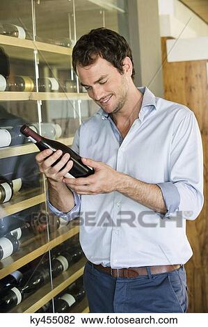 Smiling man looking at a wine bottle View Large Photo Image Stock Image - Smiling man looking at a wine bottle. Fotosearch