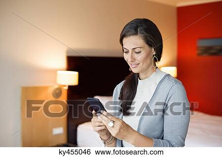 Stock Photograph - Woman using a cell phone in a hotel room. Fotosearch