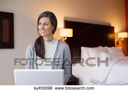 Woman using a laptop in a hotel room and smiling View Large Photo Image Stock Photo - Woman using a laptop in a hotel room and smiling. Fotosearch