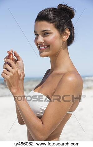 Stock Image - Beautiful woman holding a suntan lotion on the beach. Fotosearch