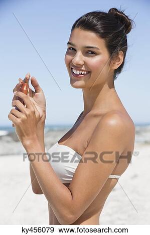 Stock Photo - Beautiful woman holding a suntan lotion on the beach. Fotosearch