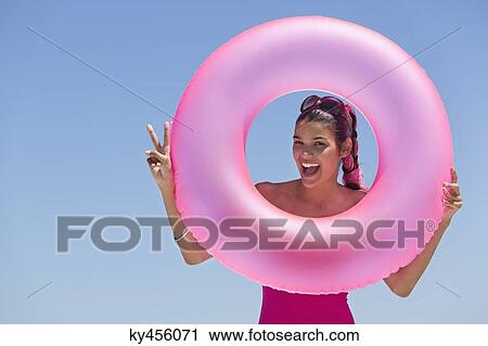 Stock Image - Beautiful woman looking through an inflatable ring on the beach. Fotosearch
