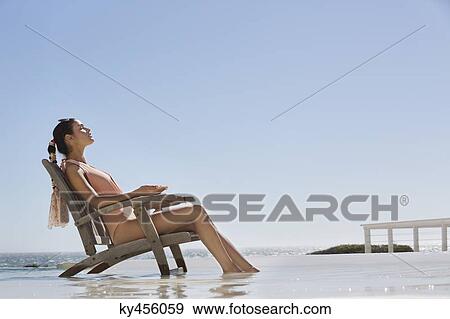 Stock Photo - Beautiful woman sitting on a chair on the beach. Fotosearch