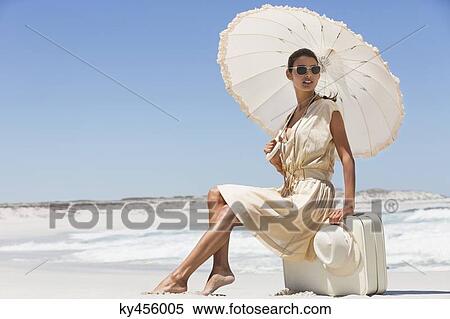 Beautiful woman sitting on a suitcase with an umbrella on the beach View Large Photo Image Stock Photography - Beautiful woman sitting on a suitcase with an umbrella on the beach. Fotosearch