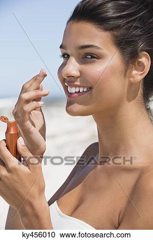 Stock Image - Beautiful woman smelling suntan lotion on the beach. Fotosearch