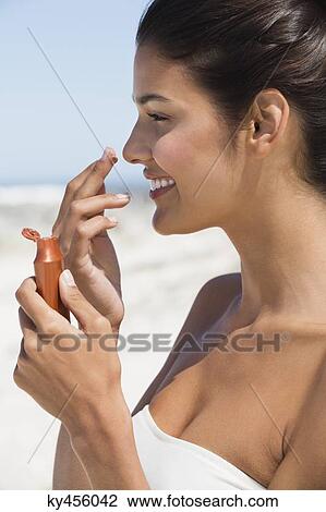 Stock Image - Beautiful woman smelling suntan lotion on the beach. Fotosearch