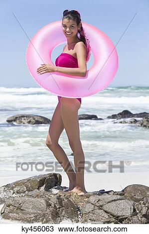 Stock Image - Beautiful woman standing with an inflatable ring on the beach. Fotosearch