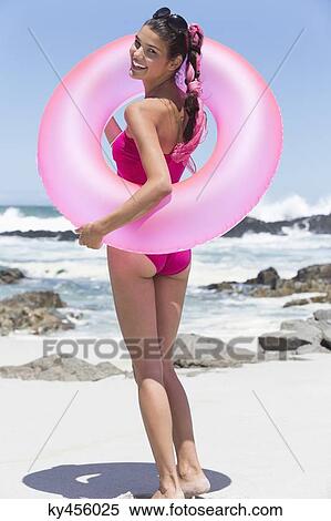 Stock Photography - Beautiful woman standing with an inflatable ring on the beach. Fotosearch