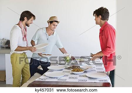 Friends arranging food on a dining table View Large Photo Image Stock Image - Friends arranging food on a dining table. Fotosearch