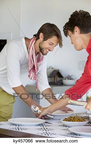 Stock Photograph - Friends arranging plates on a dining table. Fotosearch