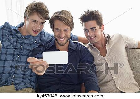 Stock Photograph - Three friends sitting on a couch and looking at mobile phone. Fotosearch