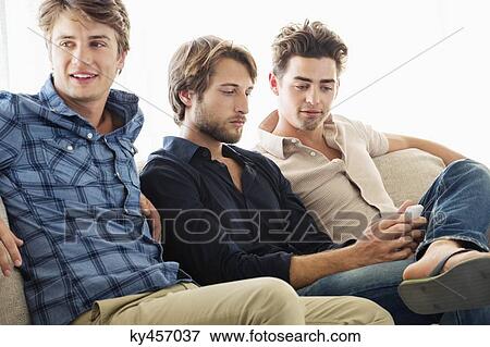 Stock Photo - Three male friends sitting together on a couch. Fotosearch