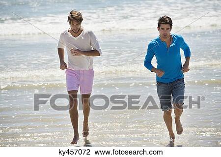 Stock Image - Two male friends running on the beach. Fotosearch