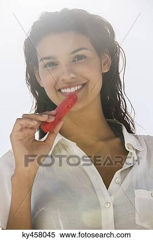 Stock Photography - Beautiful woman eating a slice of watermelon on the beach. Fotosearch