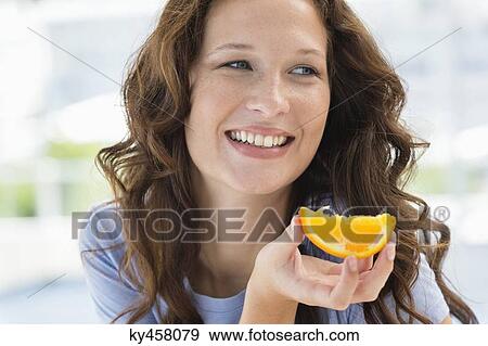 Close-up of a smiling woman holding a slice of an orange View Large Photo Image Stock Photo - Close-up of a smiling woman holding a slice of an orange. Fotosearch